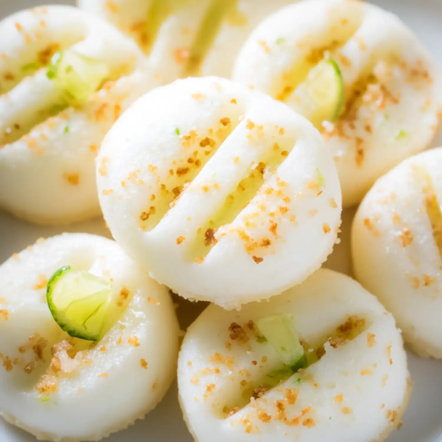 A close-up image of several white round dumplings, topped with a sprinkle of brown seasoning and garnished with small pieces of green lime.