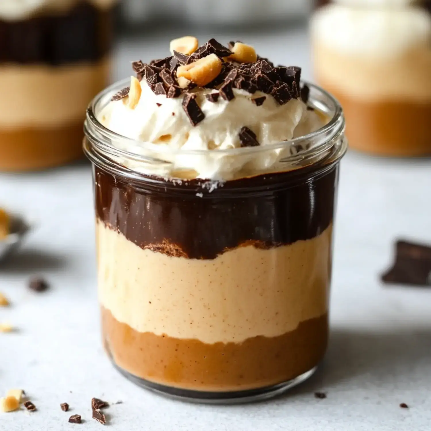 A dessert in a jar featuring layers of chocolate, peanut butter, and cream, topped with chopped chocolate and nuts.