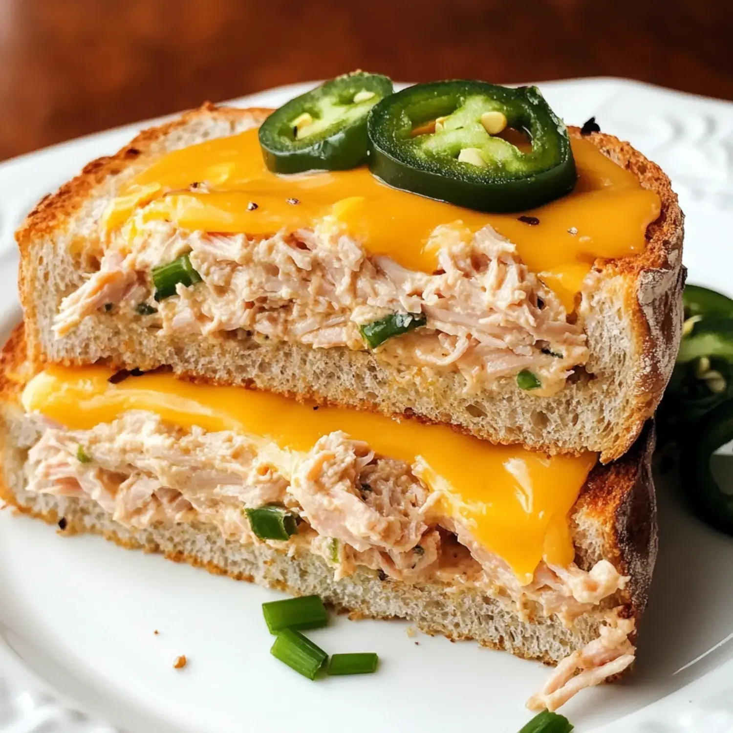 A close-up of a sliced sandwich filled with shredded chicken mixed with green onions, topped with melted cheddar cheese and sliced jalapeños.