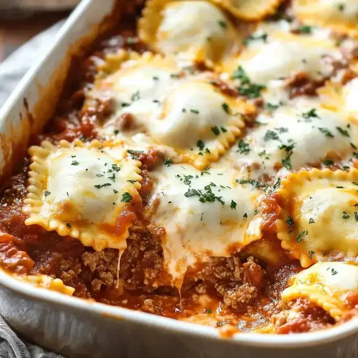 A baking dish filled with ravioli topped with melted cheese, ground meat, and garnished with parsley in a tomato sauce.