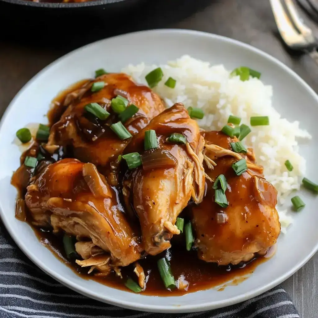 A plate of tender chicken thighs glazed with a savory sauce, garnished with green onions, served alongside fluffy white rice.