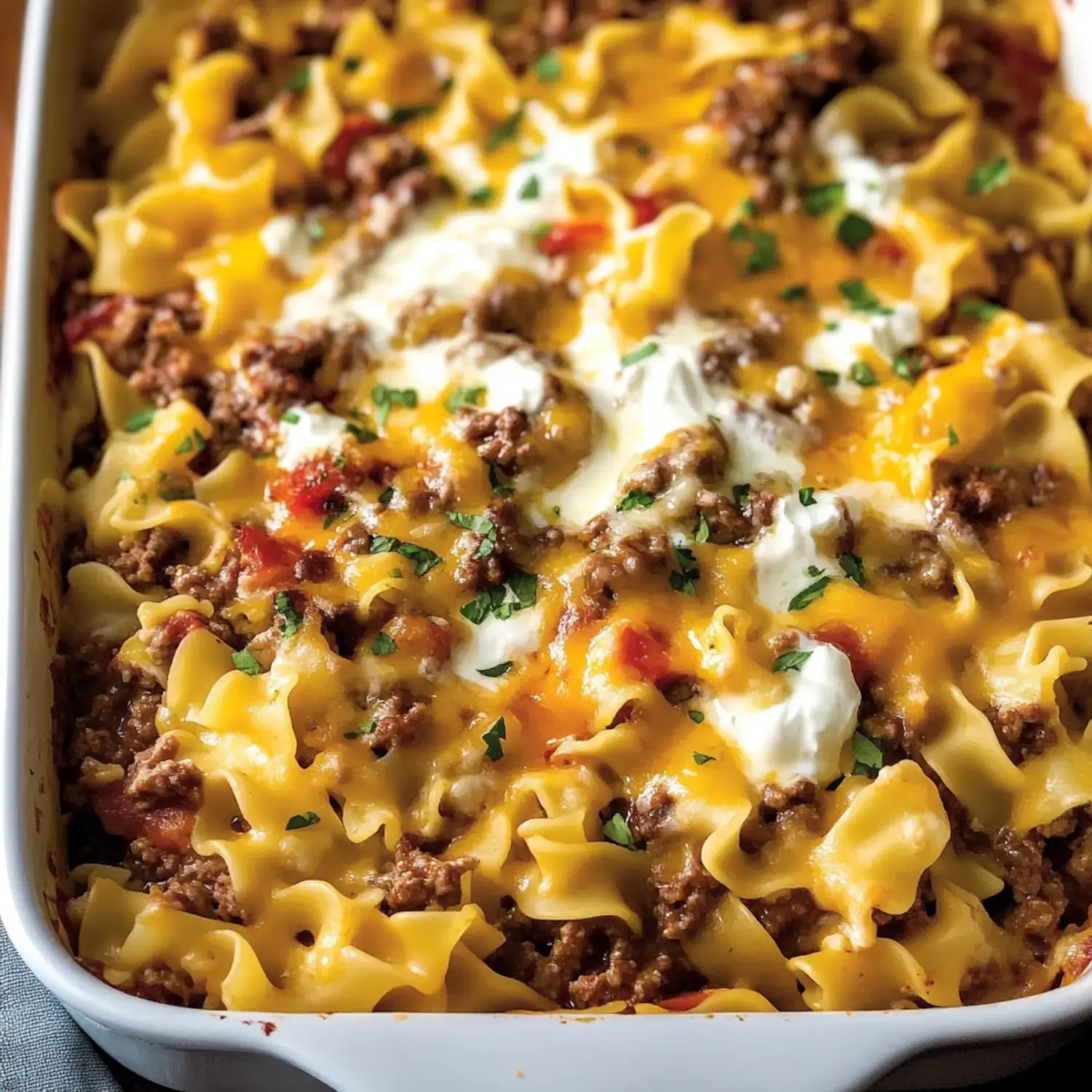 A close-up of a casserole dish filled with layered egg noodles, ground meat, melted cheese, and garnished with parsley.