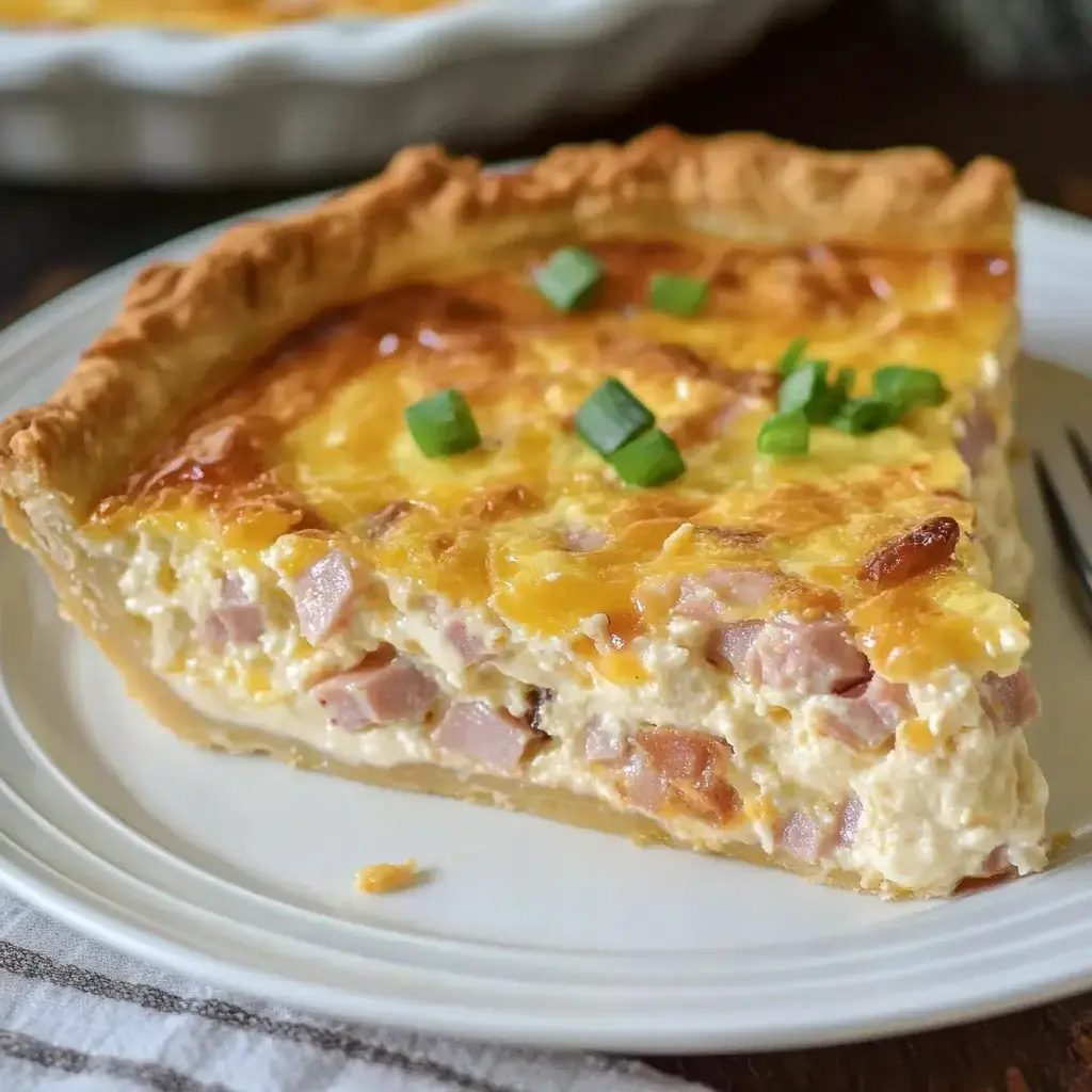 A slice of ham and cheese quiche is displayed on a white plate, garnished with green onions.