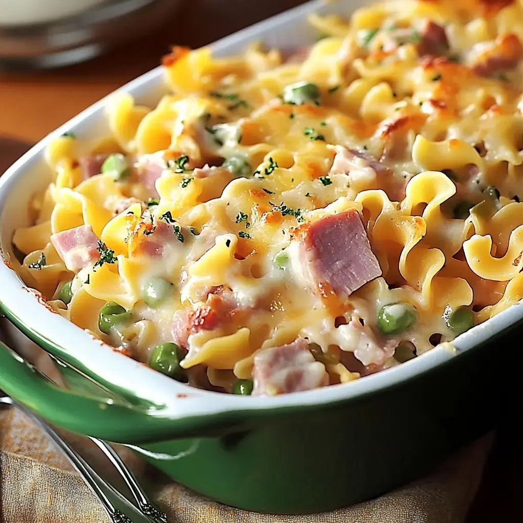 A close-up view of a casserole dish filled with creamy pasta, ham, peas, and melted cheese, garnished with parsley.