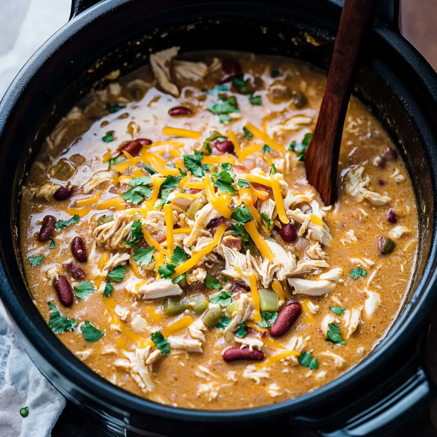 A close-up view of a pot of savory chicken chili topped with shredded cheese and fresh cilantro.