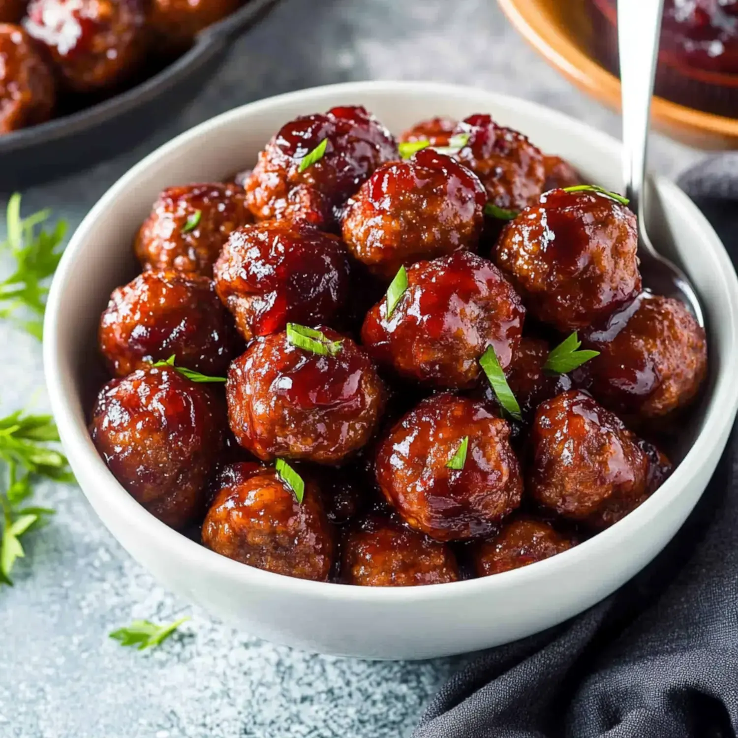 A bowl of shiny, glazed meatballs garnished with chopped herbs.