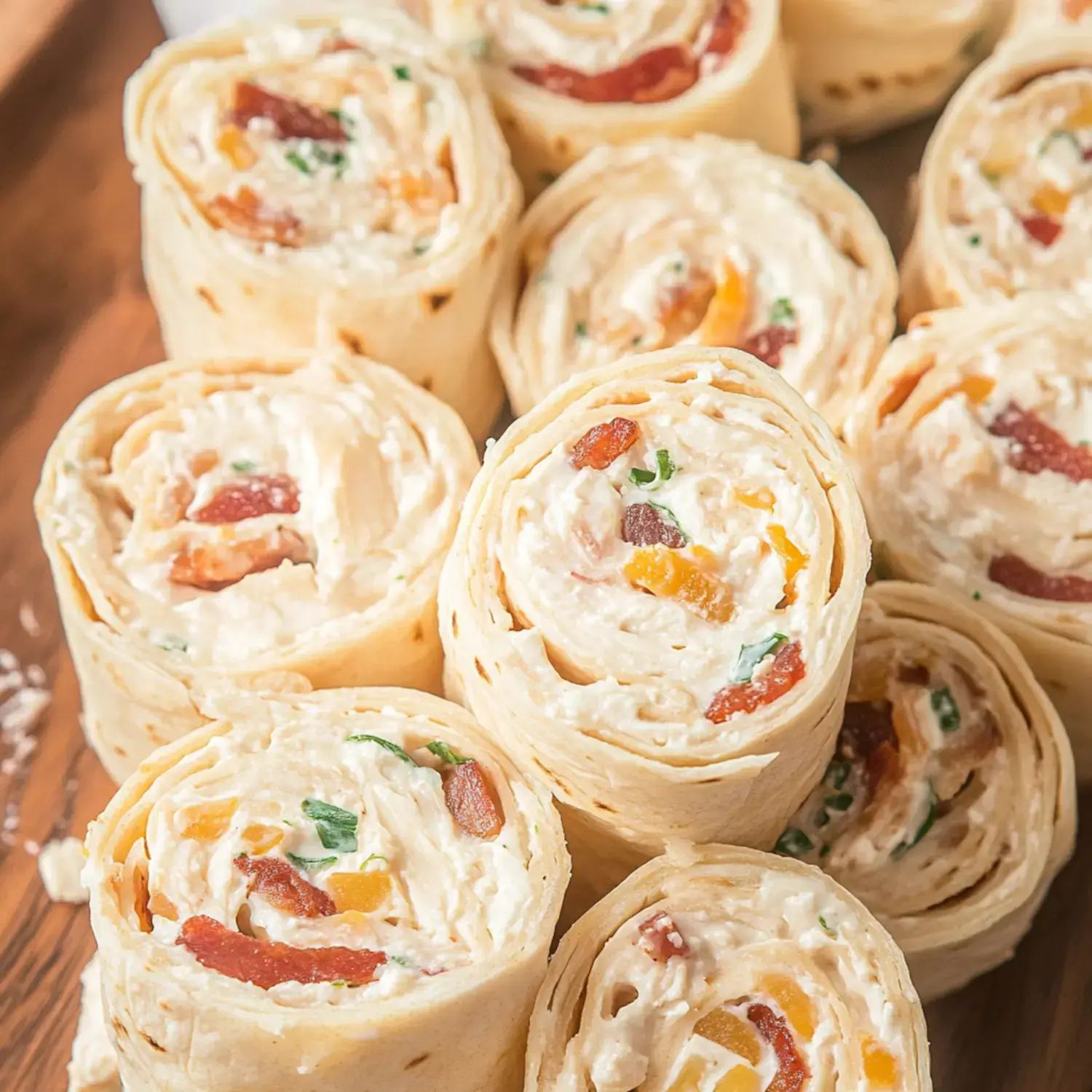 A close-up view of rolled tortilla pinwheels filled with a creamy mixture of bacon, cheese, and chopped herbs, arranged on a wooden platter.