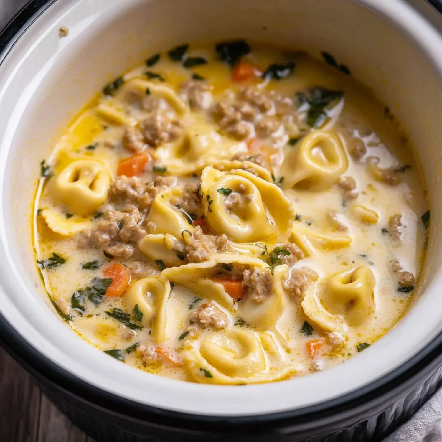 A creamy soup filled with tortellini, ground meat, and vegetables in a white bowl.