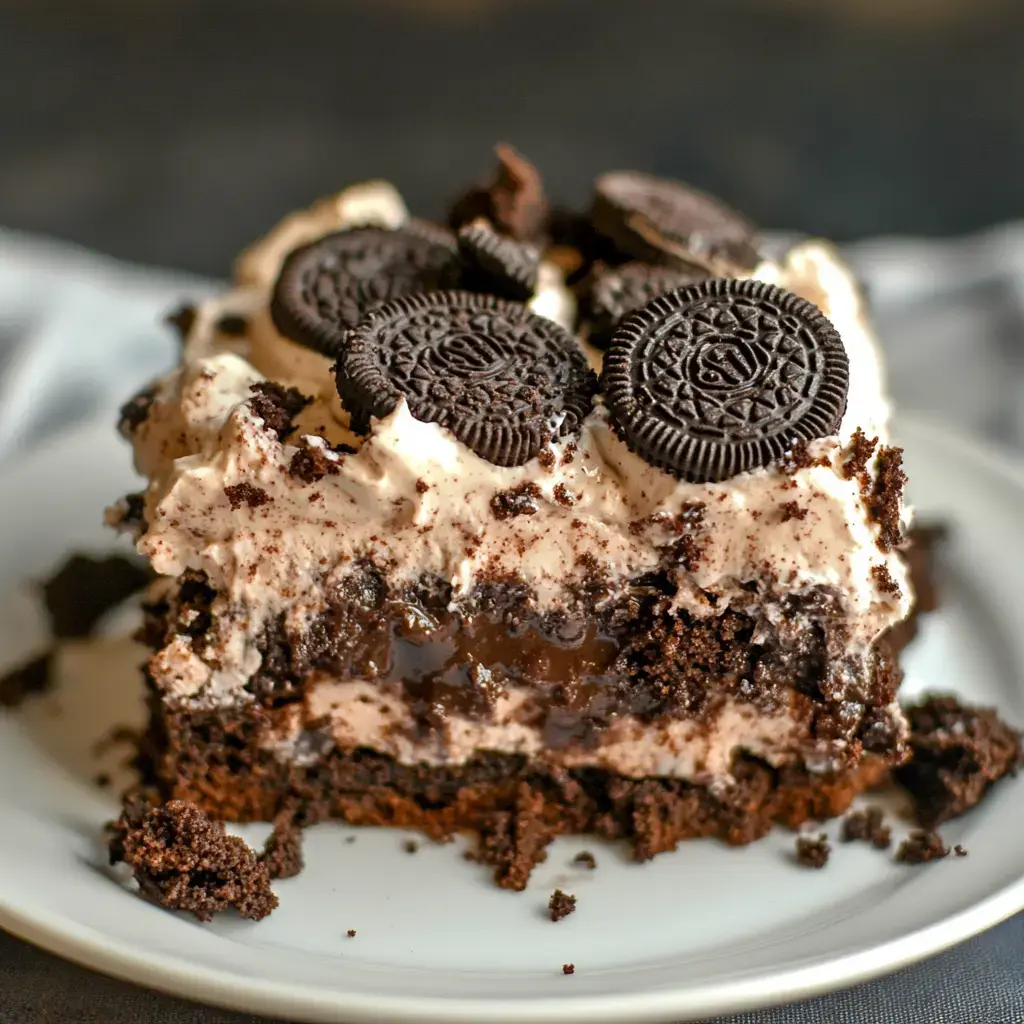 A slice of layered chocolate cake topped with whipped cream and Oreo cookie pieces.