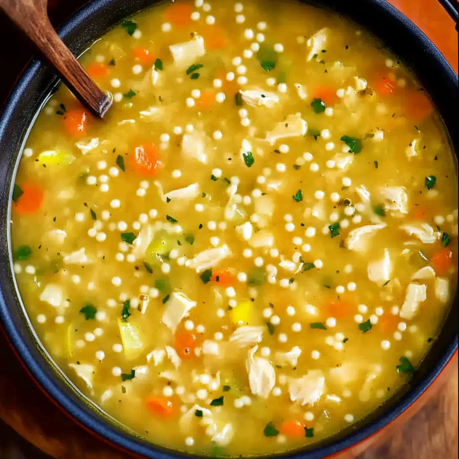 A close-up of a bowl of chicken soup featuring small pasta, carrots, and herbs.