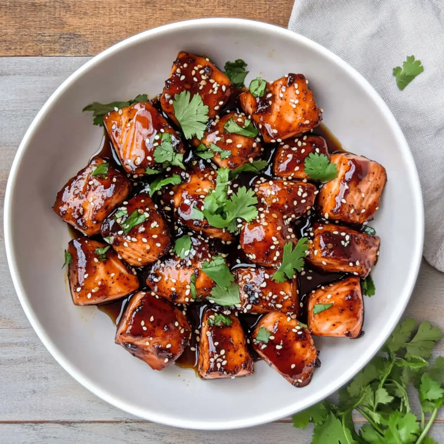 A bowl of glazed salmon cubes garnished with sesame seeds and fresh cilantro.