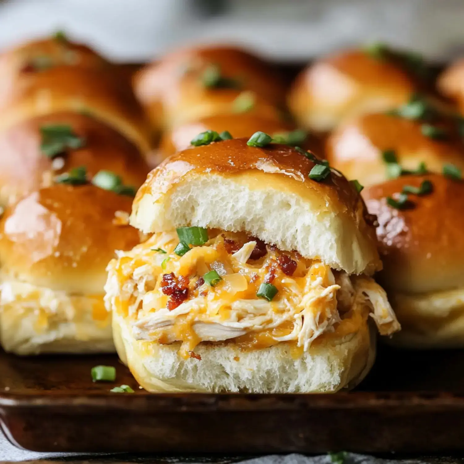 A close-up of a freshly baked chicken and cheese slider, with the top bun partially removed, revealing the filling and garnished with green onions.