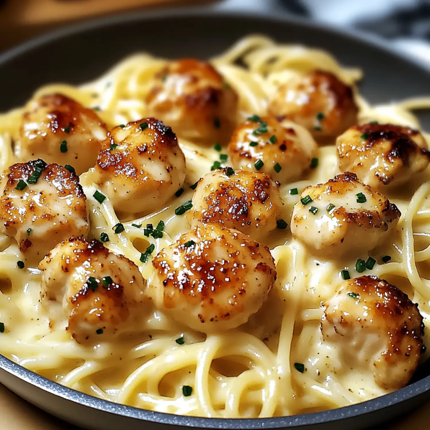 A close-up of creamy pasta with golden-brown scallops sprinkled with green chives.