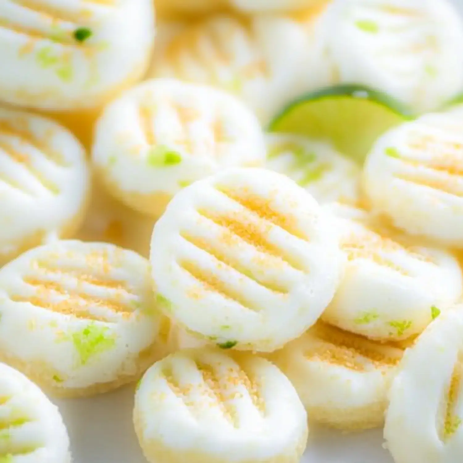 A close-up of small round confections with a white surface, featuring green flecks and a light dusting of a golden topping.