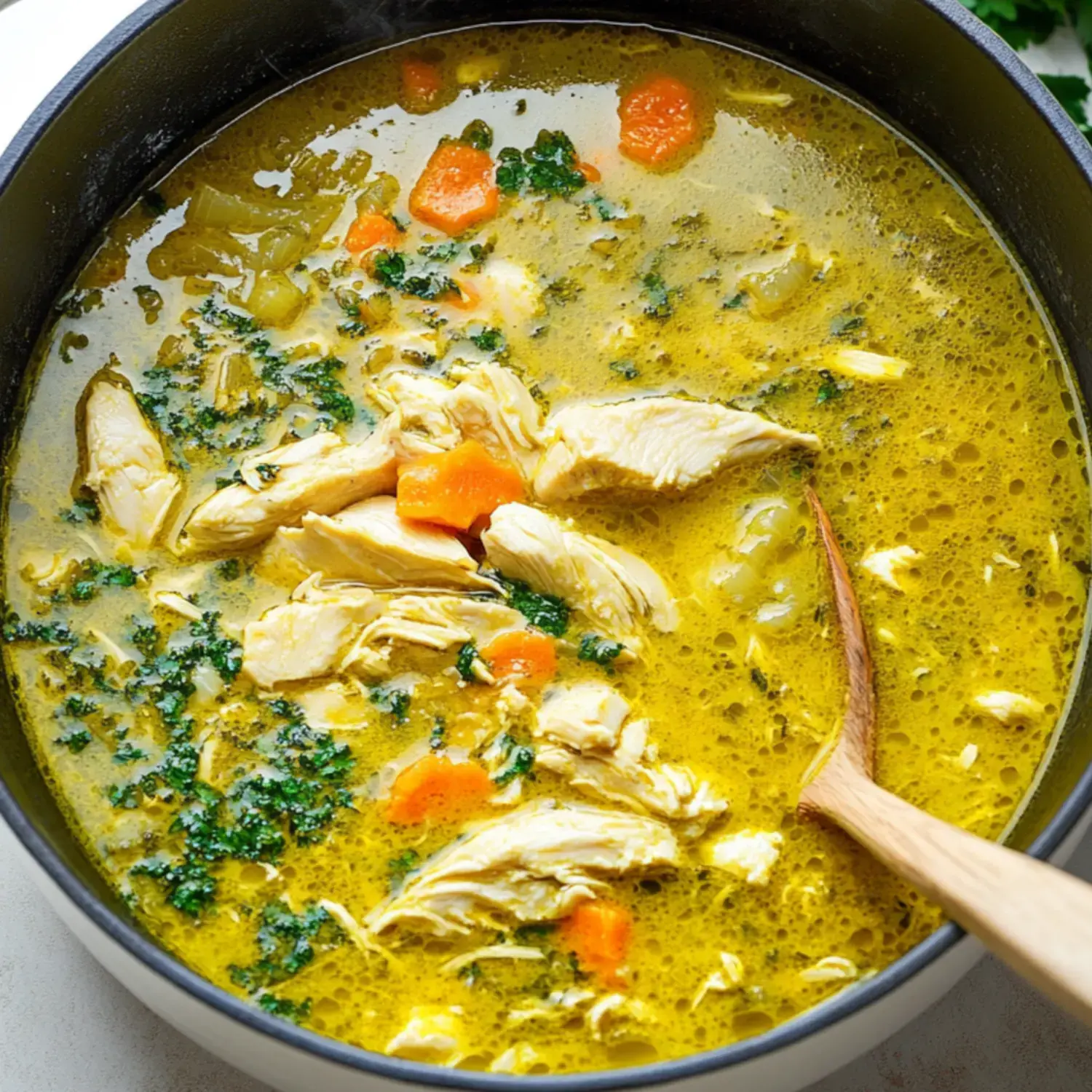 A warm pot of chicken soup with shredded chicken, carrots, and leafy greens simmering in a golden broth.