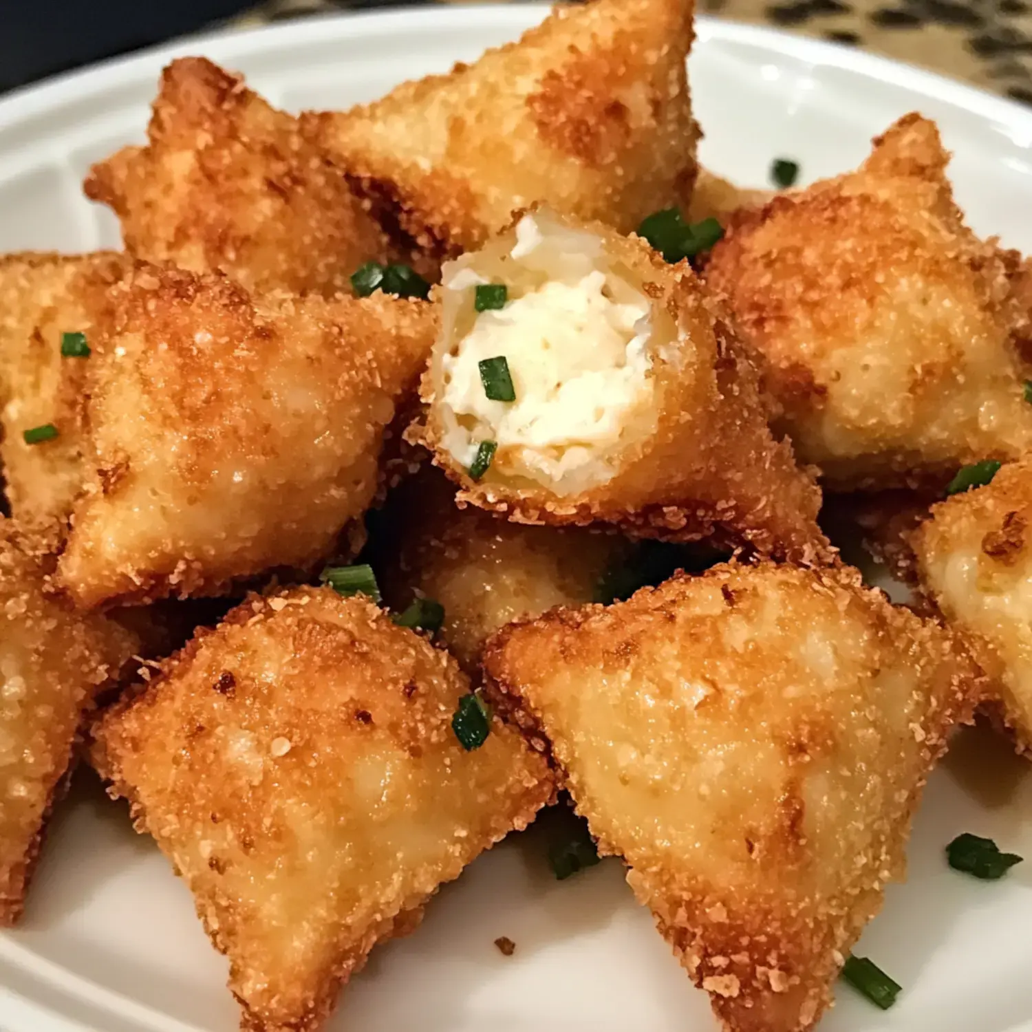 A pile of golden-brown, crispy triangular dumplings with a creamy filling, garnished with chopped green onions.