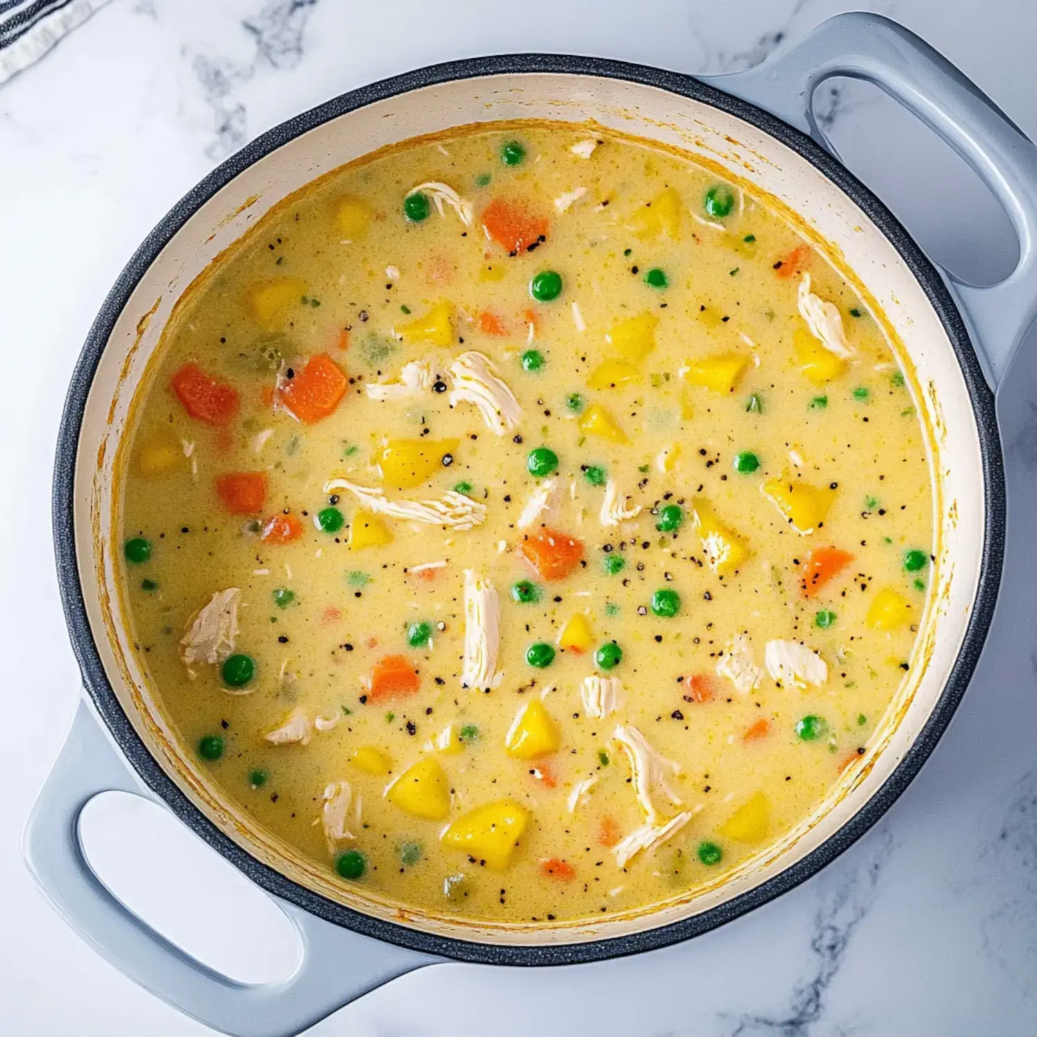 A creamy chicken and vegetable soup with carrots, peas, and yellow squash simmering in a pot.