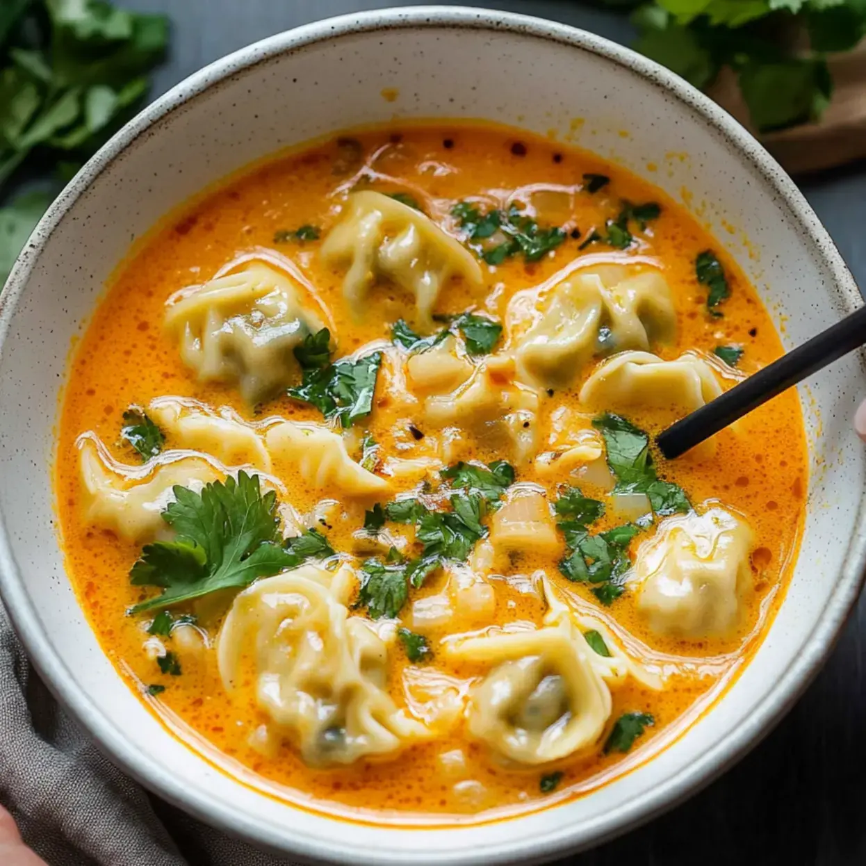 A bowl of creamy soup with dumplings and fresh cilantro.