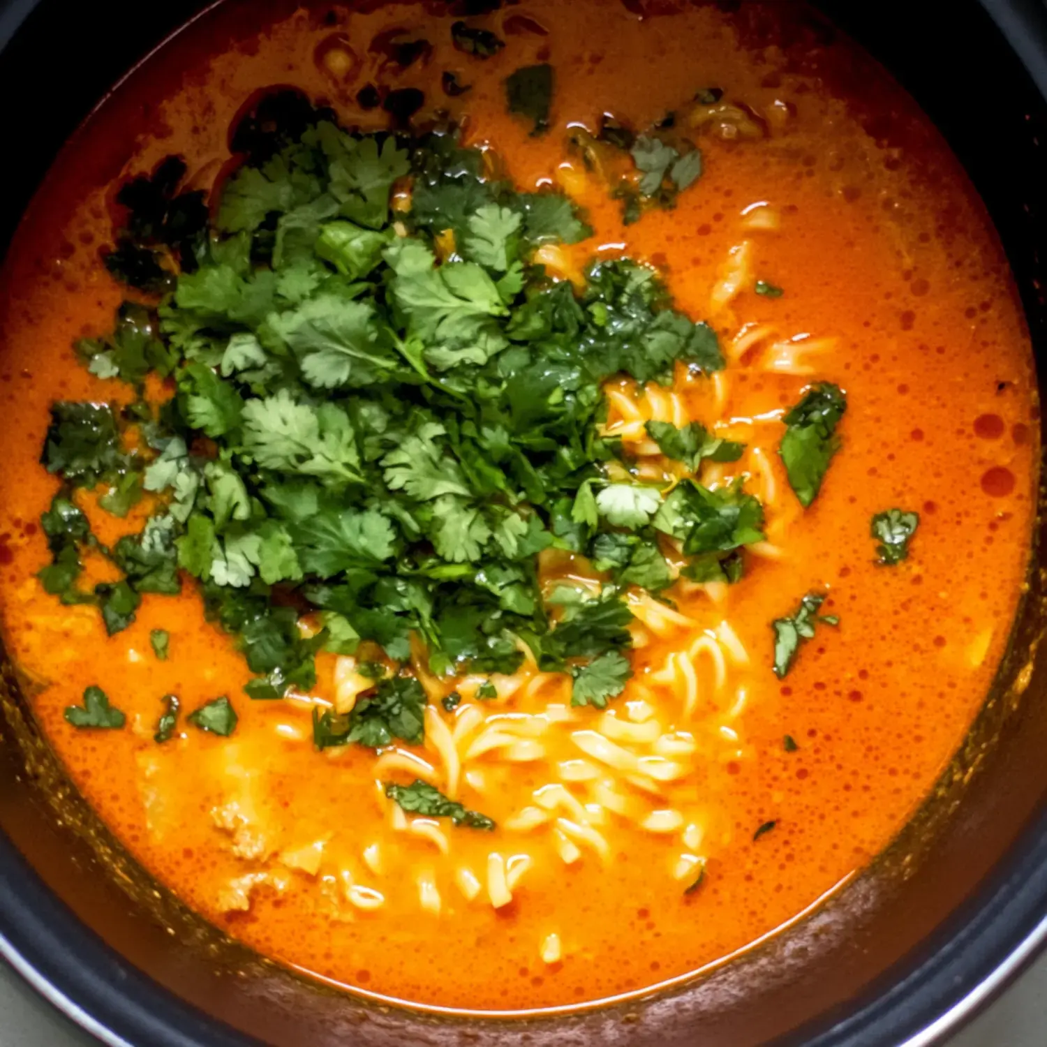 A close-up of a bowl of vibrant orange soup topped with fresh chopped cilantro and noodles.