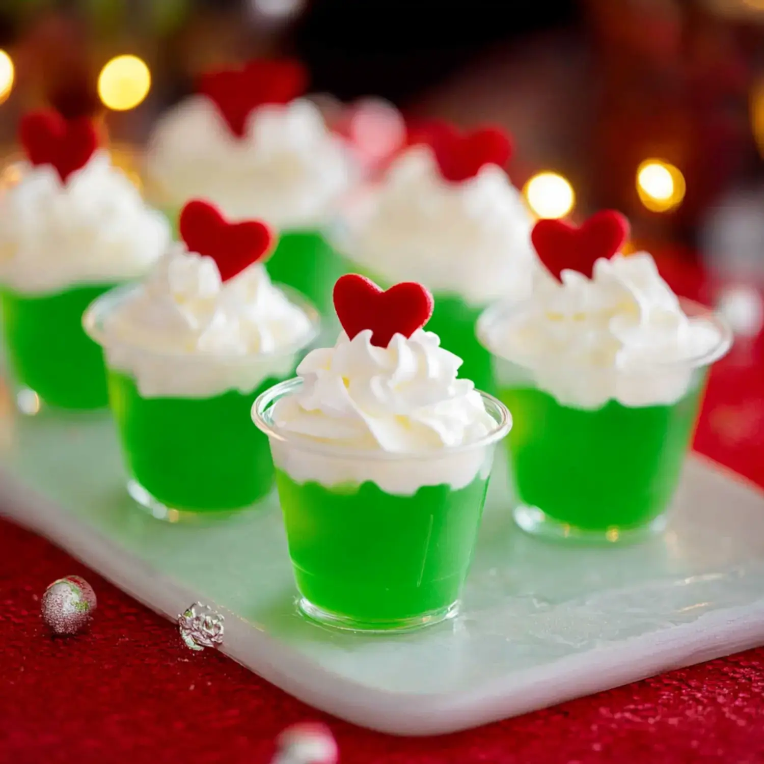 A row of green gelatin cups topped with whipped cream and red heart decorations on a festive surface.