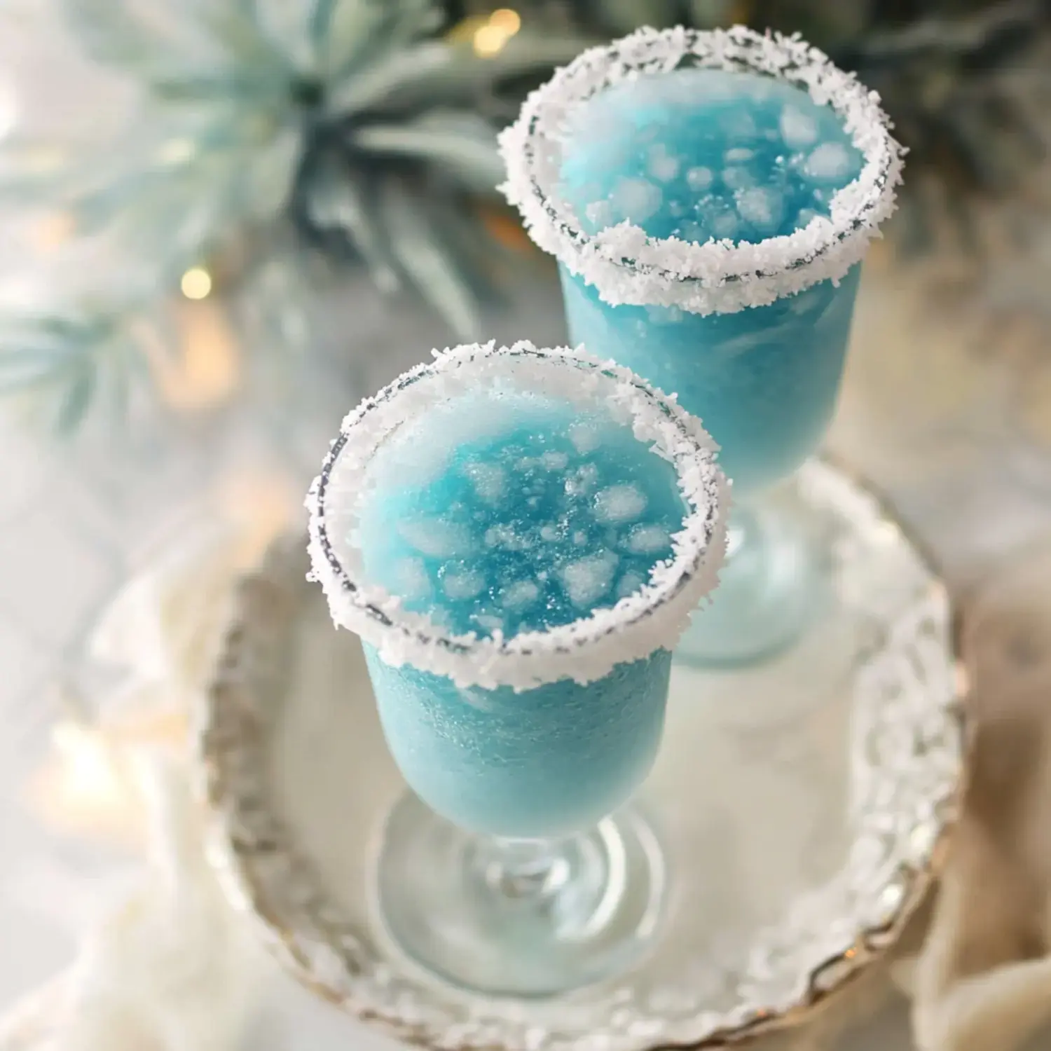 Two frosty, blue cocktails topped with icy blue slush and adorned with white sugar rims are displayed on a decorative tray.