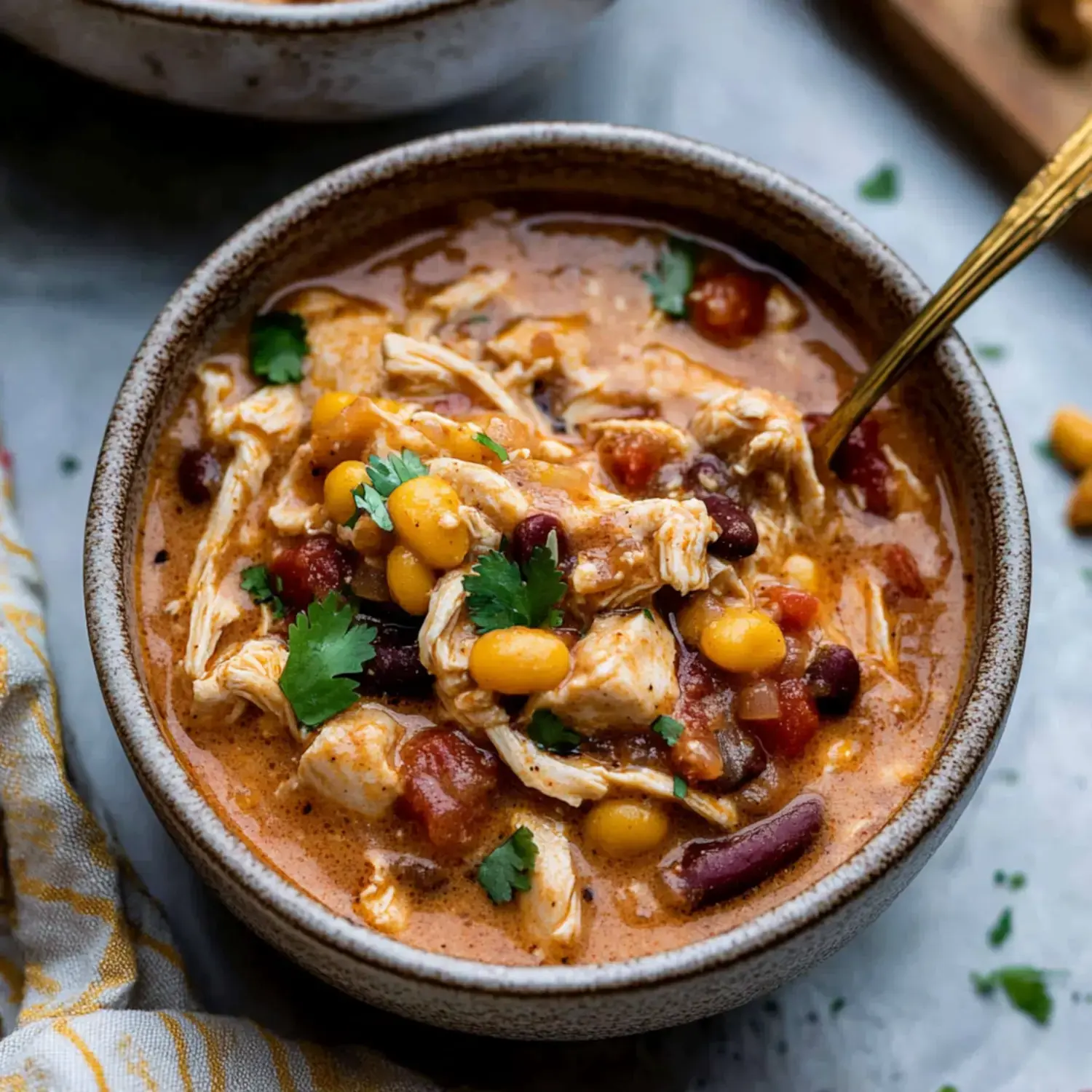 A close-up view of a bowl of creamy chicken chili garnished with cilantro and beans.