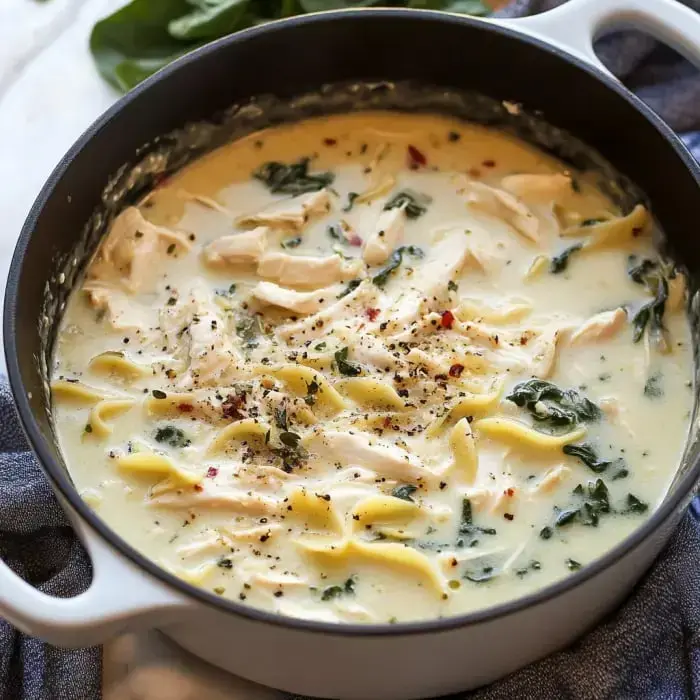 A creamy chicken noodle soup with spinach and spices simmering in a pot.