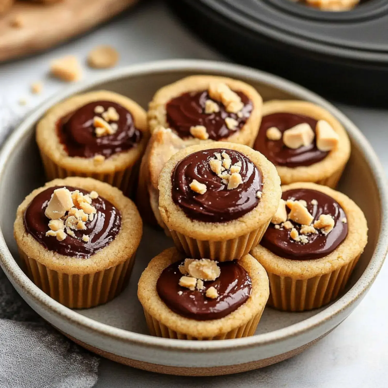 A plate of mini cupcakes topped with chocolate frosting and crushed peanuts.