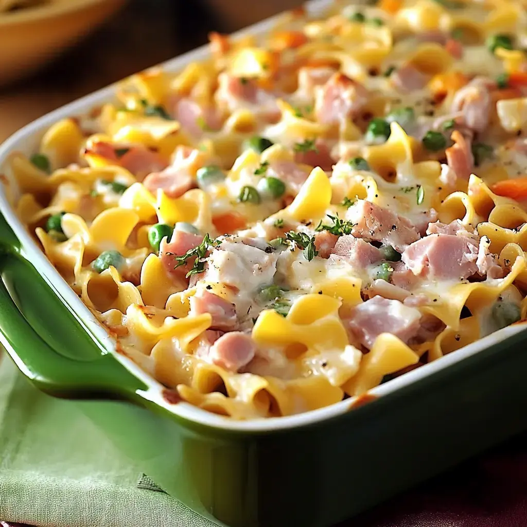 A creamy noodle casserole with ham, peas, and herbs in a green dish.