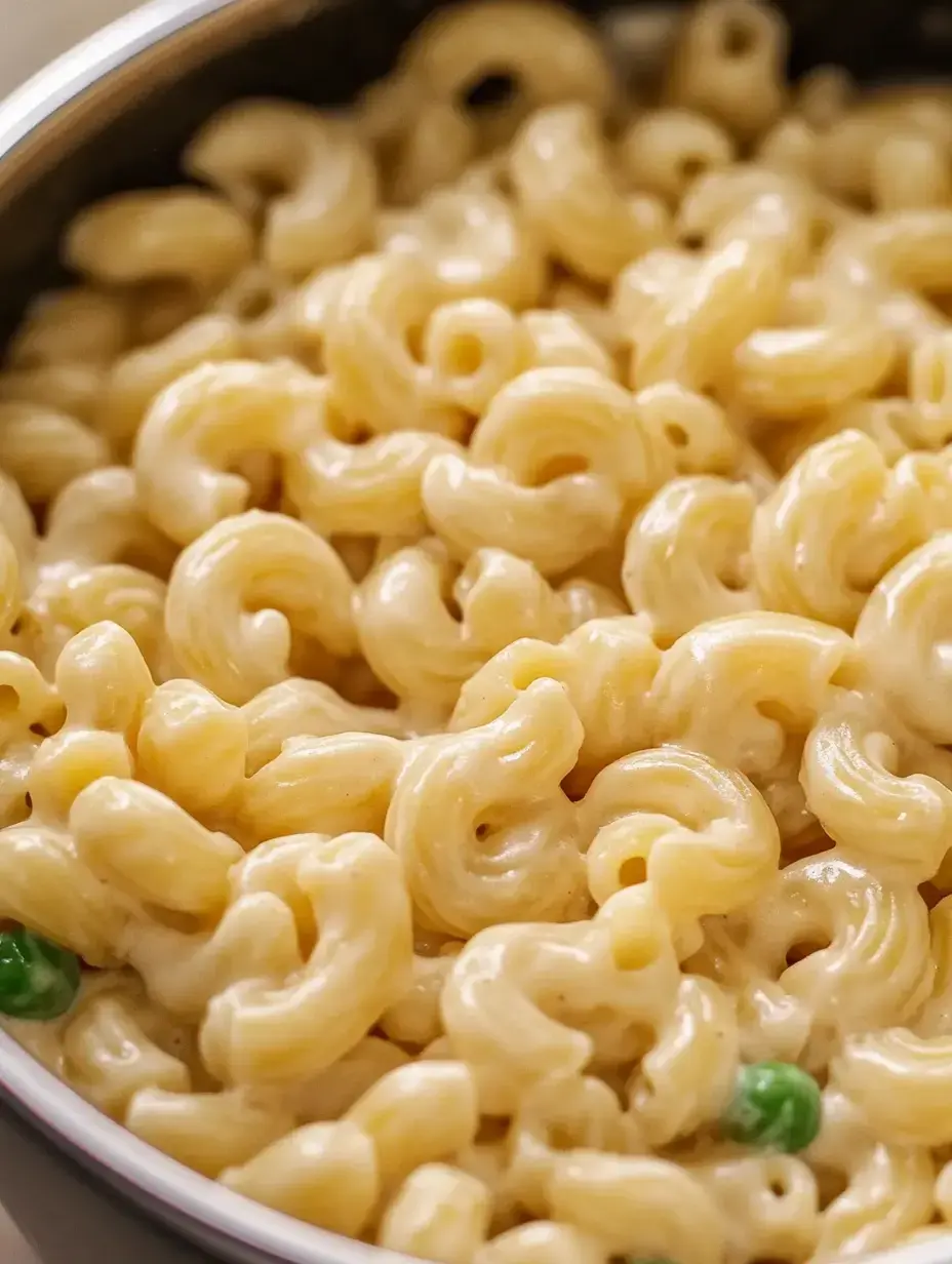 A close-up view of creamy macaroni noodles with a hint of green peas mixed in.