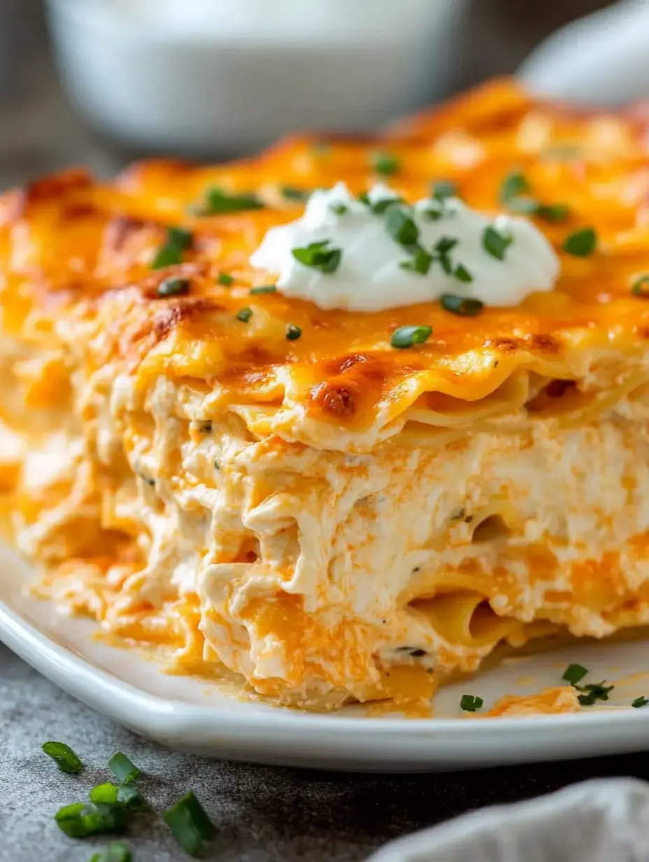 A close-up of a dish of creamy lasagna topped with cheese and garnished with sour cream and chopped green onions.