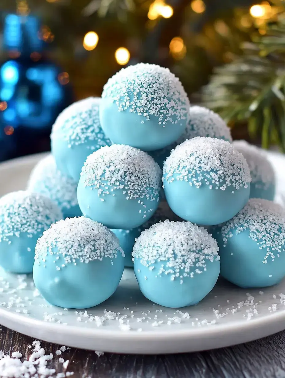 A white plate piled with snowball-shaped blue treats, adorned with sparkling sugar, sits against a softly lit background of holiday decorations.