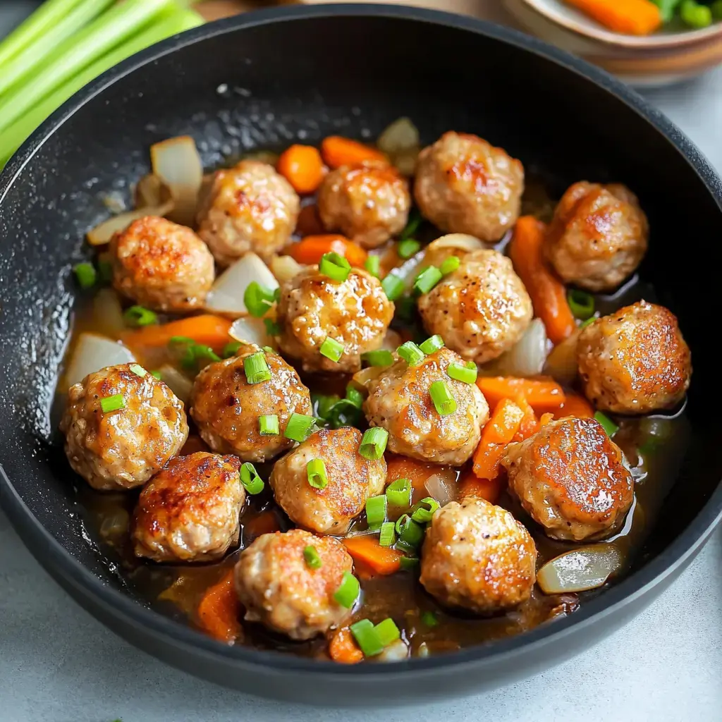 A black pan filled with savory meatballs, sliced carrots, and onions, garnished with chopped green onions in a glossy sauce.