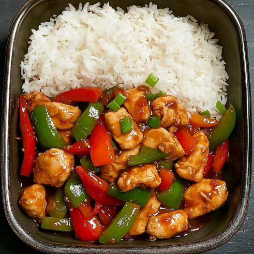 A bowl of sizzling garlic chicken stir fry with peppers and steamed rice.