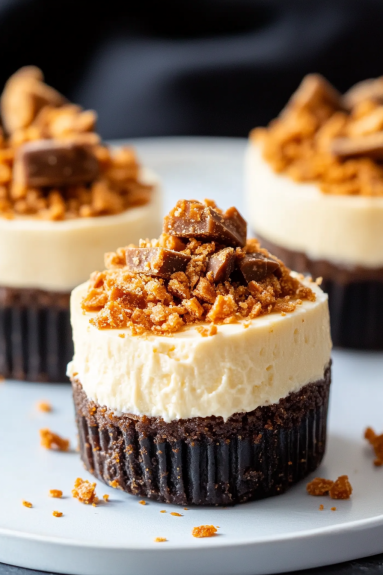 Three mini butterfinger cheesecakes on a plate.