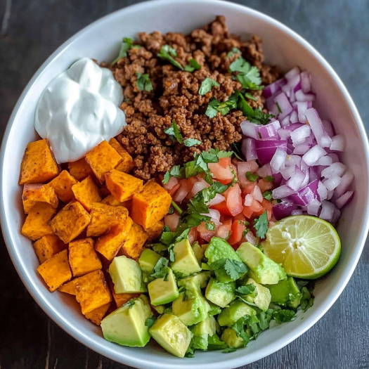 A bowl filled with a colorful assortment of ingredients, including sweet potatoes, avocado, tomatoes, onions, and lime, creates a delicious and nutritious Sweet Potato Taco Bowl.
