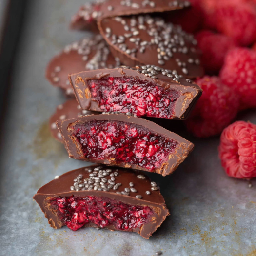 A close up of a chocolate and raspberry treat with a sprinkle of nuts on top.