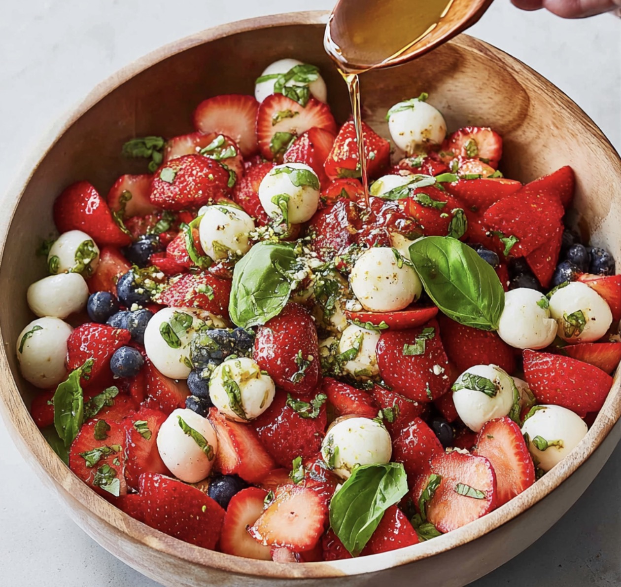 A bowl of fruit salad with strawberries, blueberries, and whipped cream.