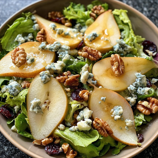A Barefoot Contessa Pear and Blue Cheese Salad is displayed in a bowl, featuring sliced apples, walnuts, and blue cheese.