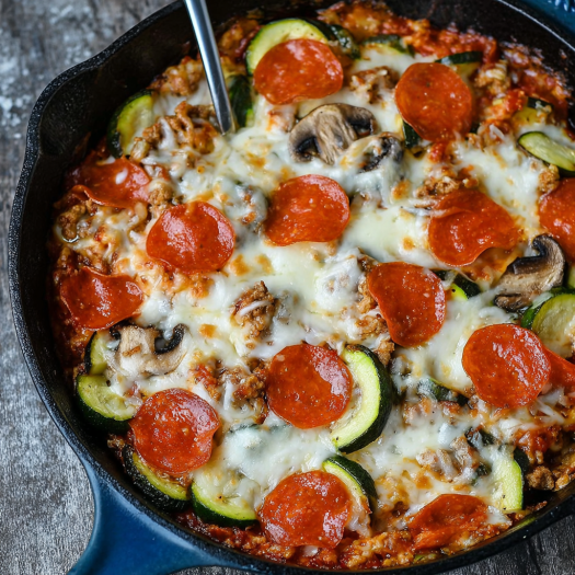 A delicious pizza with pepperoni, mushrooms, and zucchini toppings, served in a black pan.