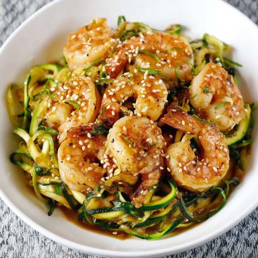 A bowl of stir fry teriyaki shrimp with zucchini noodles.