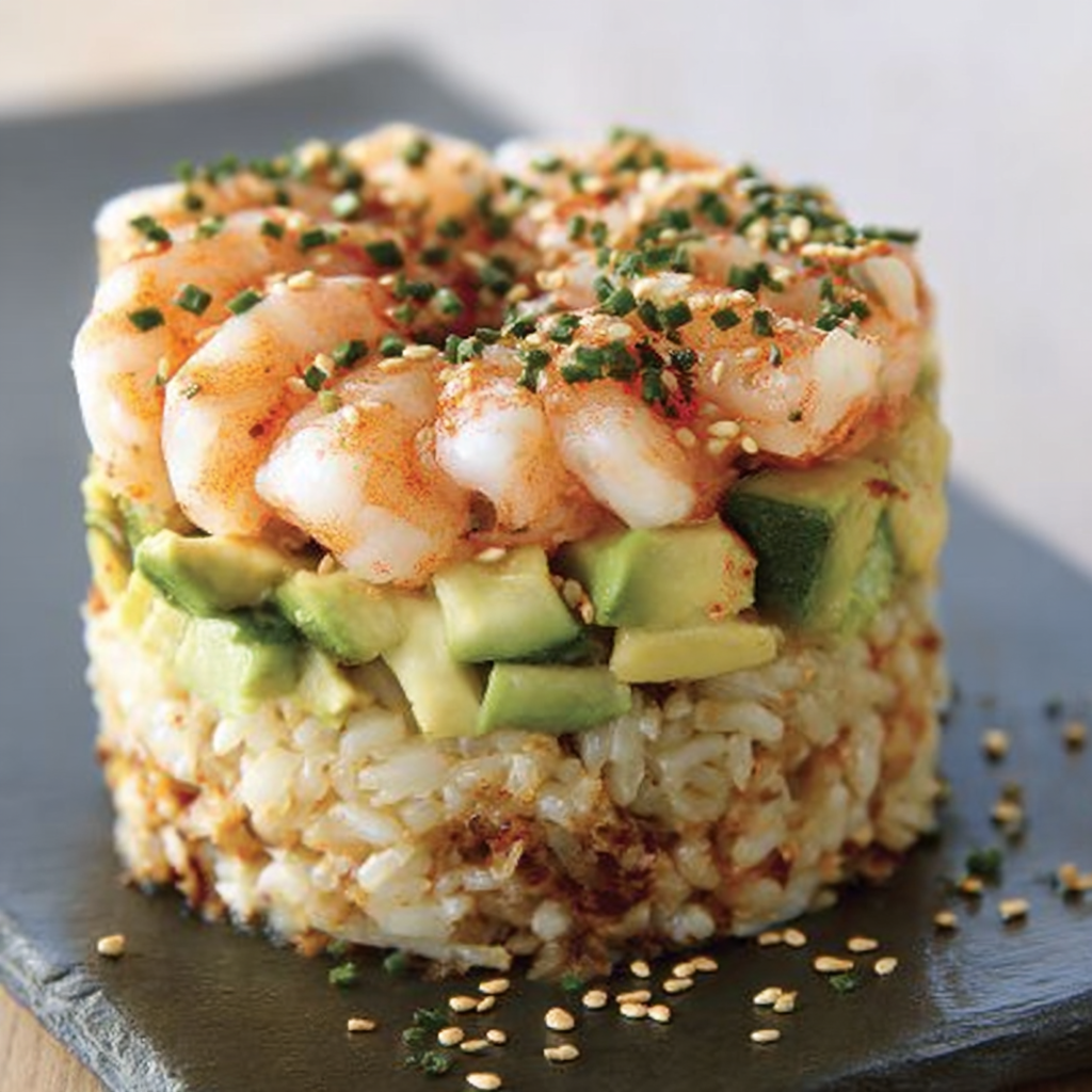 A rice dish with shrimp, avocado, and spices on a black plate.