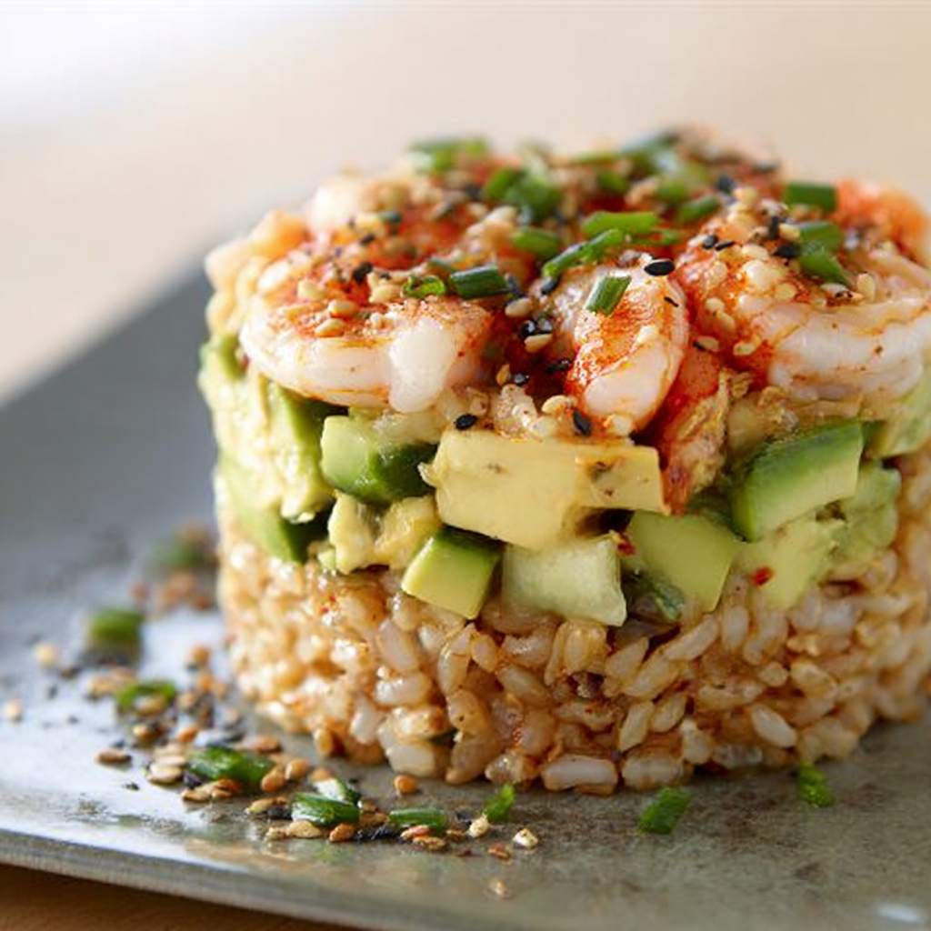 A plate of food with rice, shrimp, and avocado, topped with a spicy sauce.