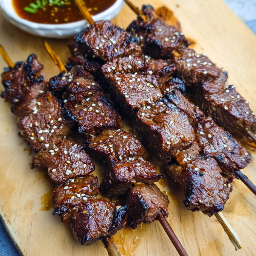 A delicious Teriyaki Sesame Beef Skewers recipe is displayed on a wooden cutting board.