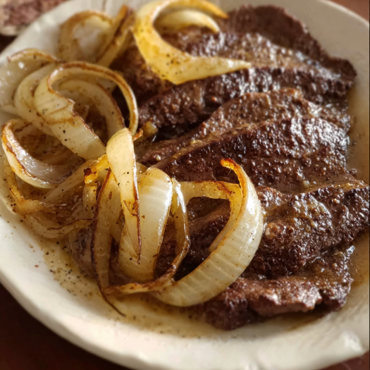 A plate of meat with onions and gravy on top.