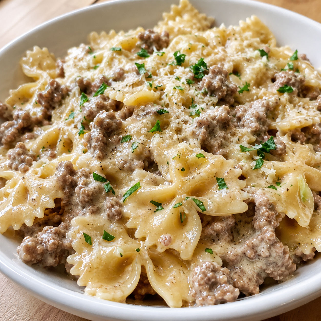 Creamy bowtie pasta with ground beef and Parmesan in a shallow white bowl