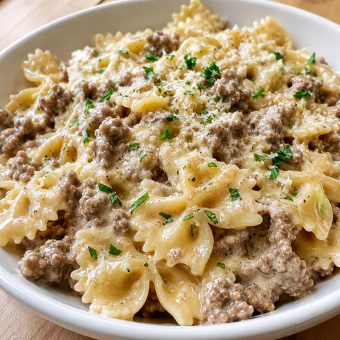 Creamy bowtie pasta with ground beef and Parmesan in a shallow white bowl