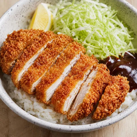 Sliced crispy chicken katsu over steamed rice with cabbage and tonkatsu sauce