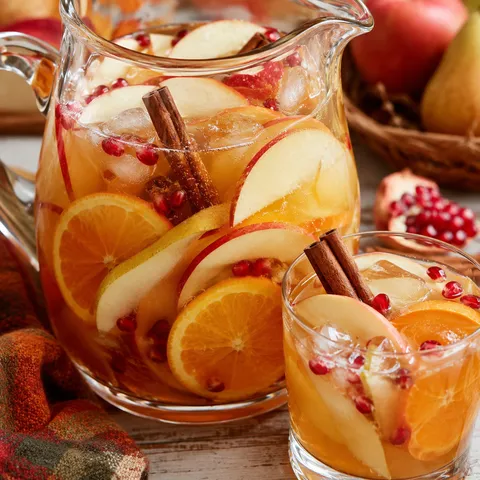 Apple cider sangria with apples, oranges, cinnamon sticks, and pomegranate seeds