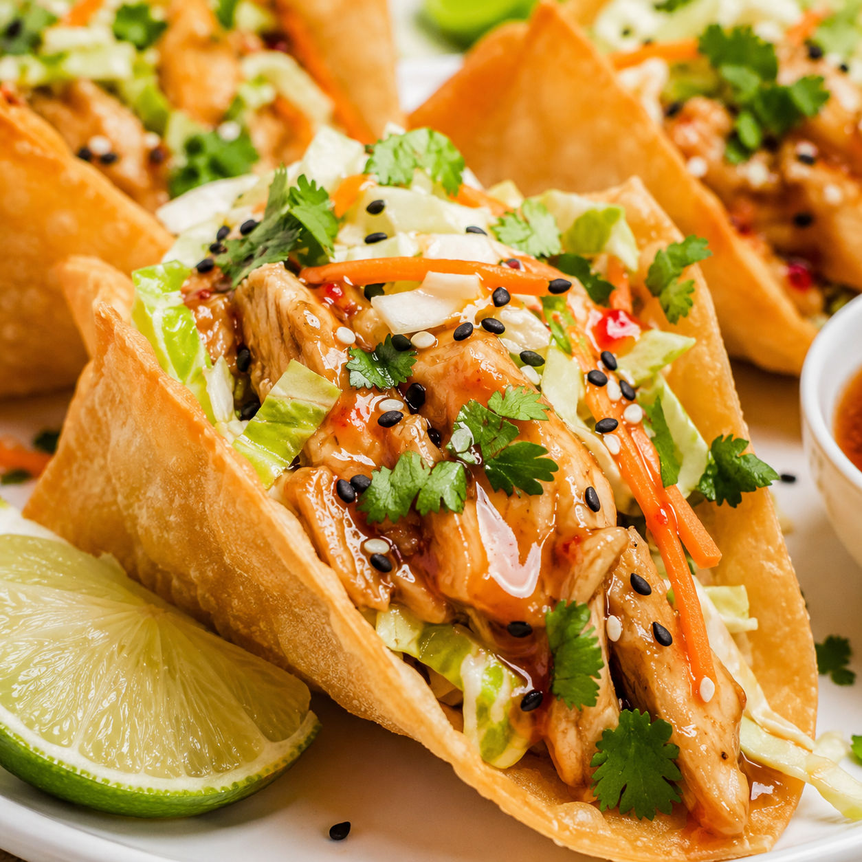 Asian chicken wonton tacos with slaw, cilantro, sesame seeds, and chili sauce